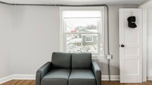 Ein Zimmer mit einem grauen Sofa, einer weißen Tür, an der eine schwarze Tasche hängt, und einem Fenster mit Blick auf einen verschneiten Hof.