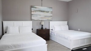 A hotel room with two white beds, a small wooden nightstand, a lamp, and a painting on the wall. - Micro Motel 2 Bed! Su (Nashville)