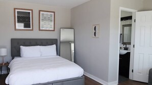 Ein Schlafzimmer mit einem Bett, einem Nachttisch, einem Spiegel und einer Tür zu einem Badezimmer.