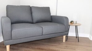 Un canapé gris aux pieds en bois et une petite table ronde agrémentée d’une plante et d’un récipient en métal.