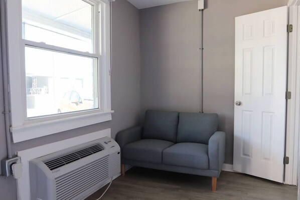 A corner room with a grey sofa, a white door, and a window with blinds.