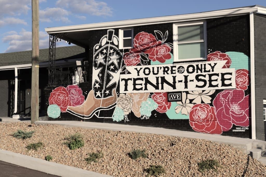 Ein Gebäude mit Wandmalerei, die eine Hand, Rosen und den Text 'YOU'RE ONLY TENN-I-SEE AVE' zeigt.