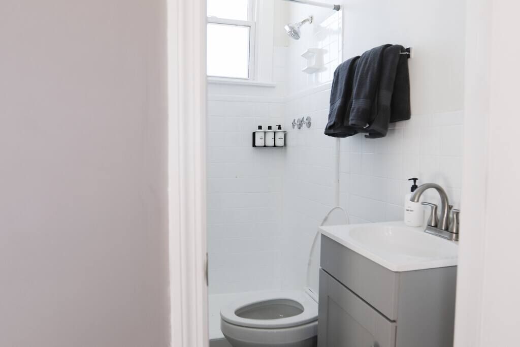 A modern bathroom with a toilet, a sink, and a shower. There are toiletries on the wall and a towel hanging on the wall.