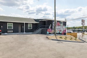 A building with a staircase leading to a second floor, a parking lot in front, and a mural on the side.