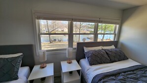 A bedroom with two beds, a window with a view of a lake and houses, and bedside tables with lamps. - Lake Front, Family fun- Sleeps 8, Newly modern remodeled 3bed/2bath private dock (Creal Springs)