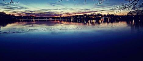 A calm lake at dusk with reflections of the sky and distant trees.