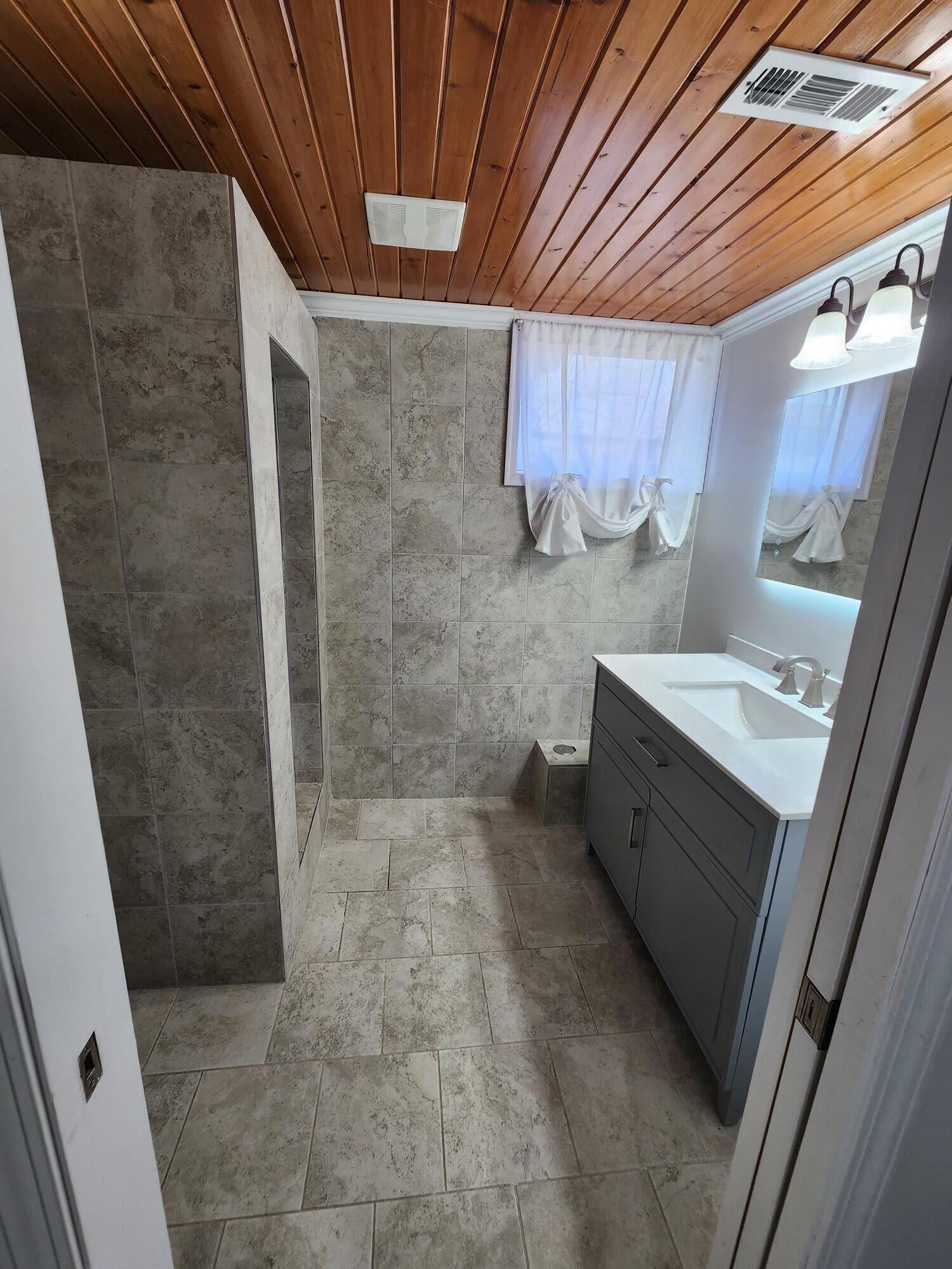 A bathroom with a wooden ceiling, a sink with a mirror, and a shower area.