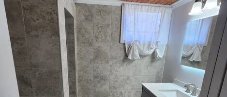 A bathroom with a wooden ceiling, a sink with a mirror, and a shower area.