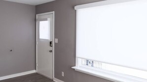Ein Zimmer mit grauen Wänden, einer weißen Tür und einem großen Fenster mit Jalousien.