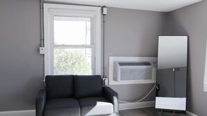 Ein modernes Zimmer mit einem grauen Sofa, einem großen Fenster und einer Klimaanlage.