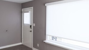 Una habitación con una puerta, una ventana con persianas y un interruptor de luz en la pared.