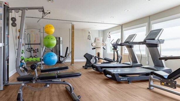 Uma academia com esteiras, supino e diversos bolas de exercícios.