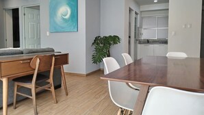En moderne stue med et træbord, hvide stole, en grå sofa og et stort abstrakt billede på væggen.