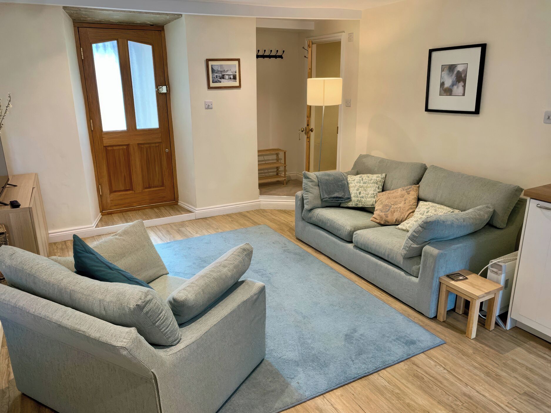 A living room with a grey sofa, a smaller grey armchair, a blue rug, and a wooden side table.