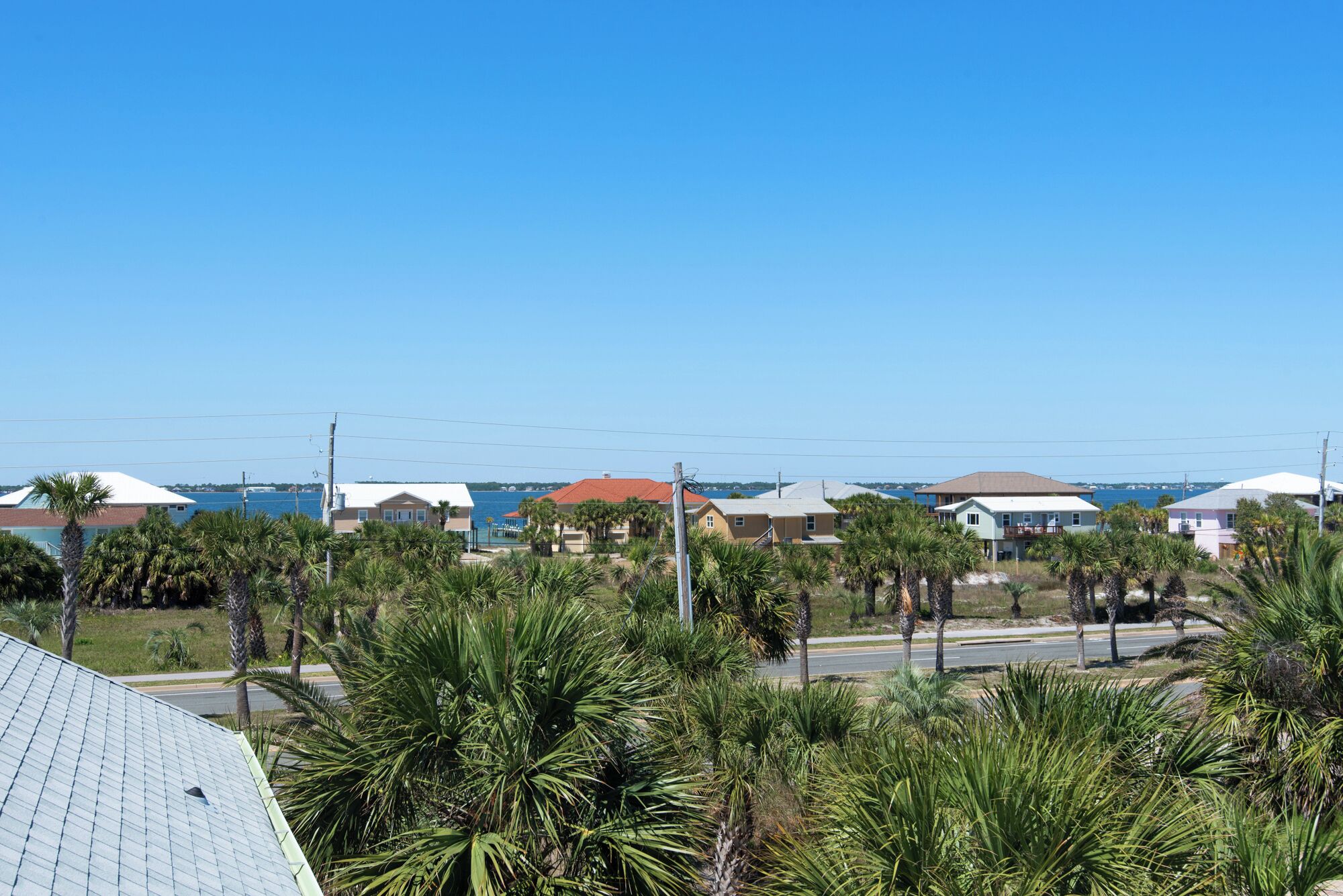 A coastal residential area with houses, palm trees, and a clear blue sky.