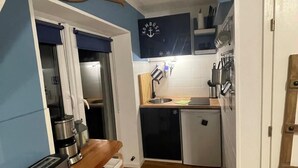 A compact kitchen with a toaster, a small refrigerator, and a wooden spoon hanging on the wall.