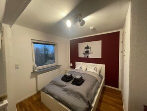 Une chambre à coucher comprenant un lit, une fenêtre, un radiateur et une œuvre d’art accrochée au mur.