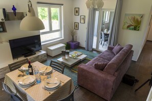 Una sala de estar con televisor, sofá, comedor y ventana con cortinas.