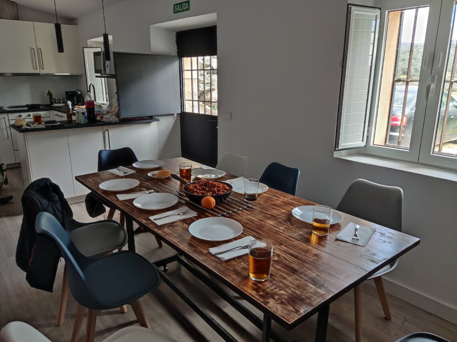 Un coin repas avec une table en bois dressée pour quatre personnes, des chaises et une vue sur l’extérieur par une fenêtre.
