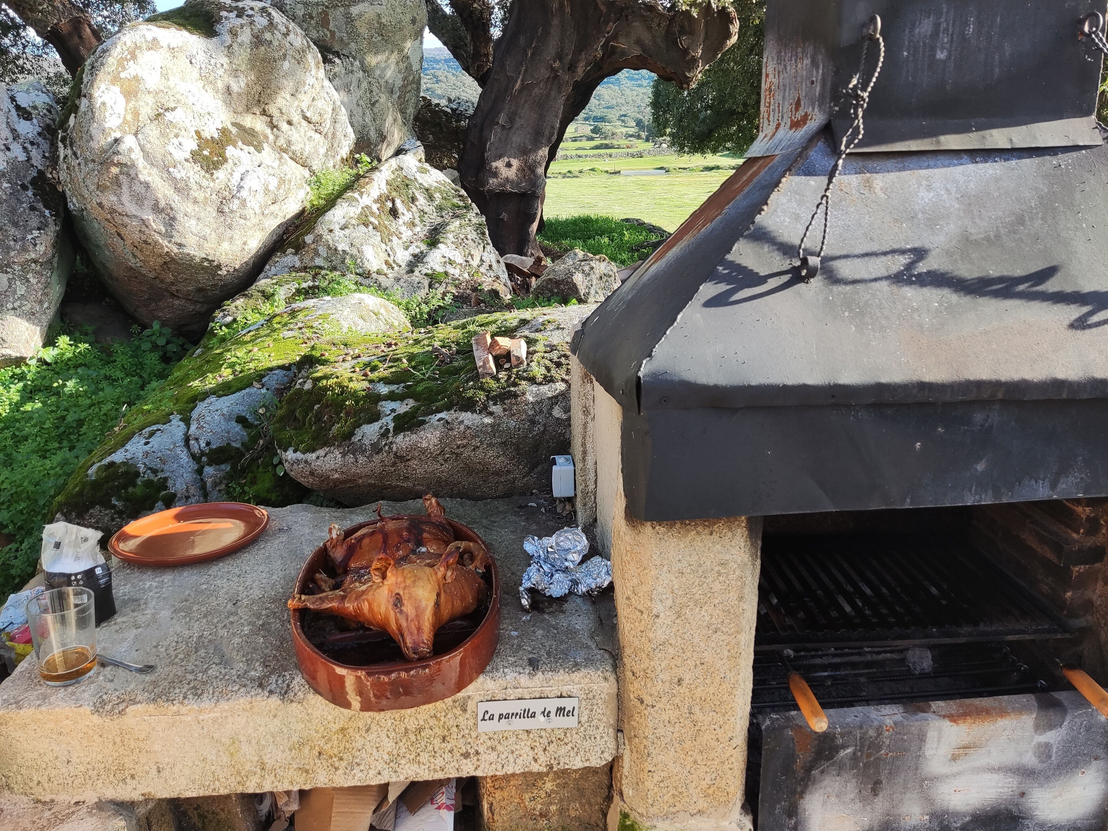 Un espace de cuisson extérieur rustique, avec un grand rocher, un saladier en bois et une étiquette indiquant : « La parrilla de Mel ».