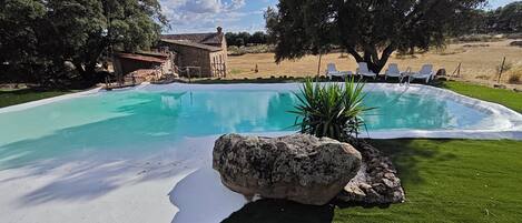 A swimming pool with a stone structure in the background, surrounded by grass and trees.