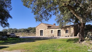 Una casa de piedra con techo de tejas, rodeada por un césped y árboles.