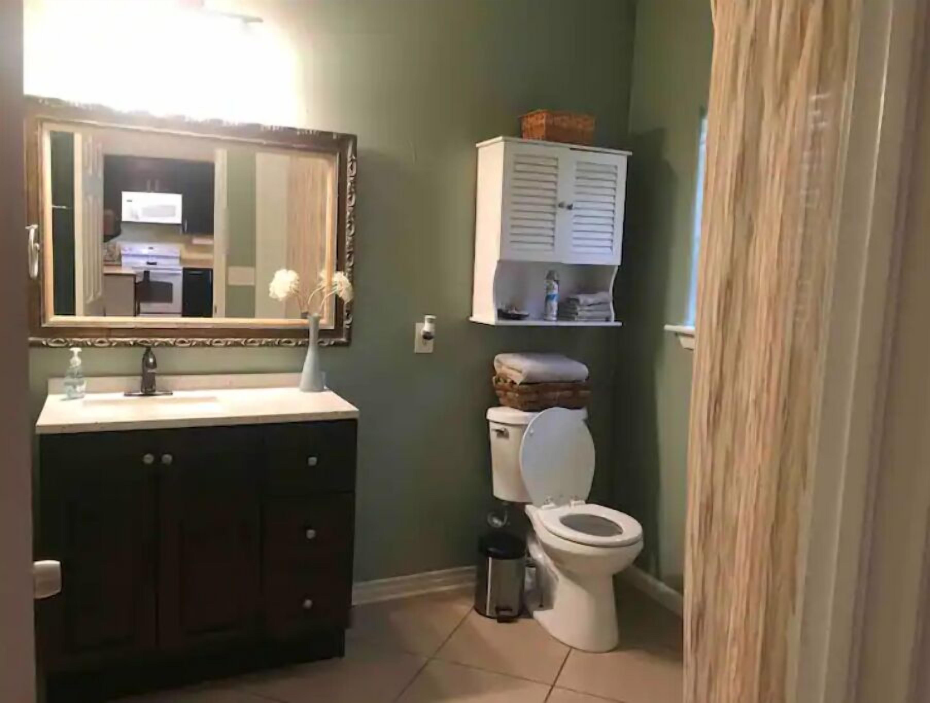 Un baño con tocador de madera oscura, inodoro blanco y espejo con marco decorativo.