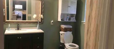 Un baño con tocador de madera oscura, inodoro blanco y espejo con marco decorativo.