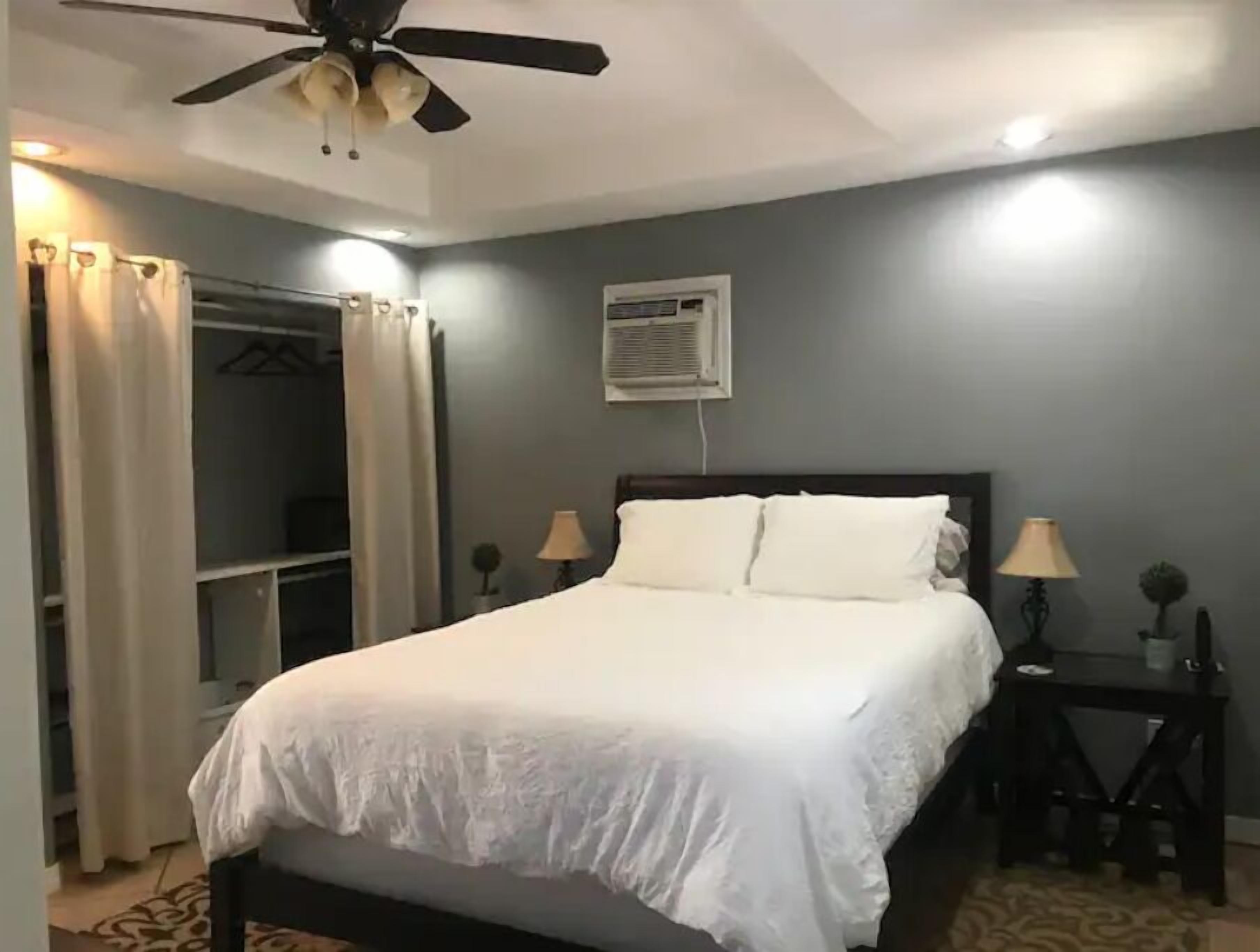A bedroom with a bed, a ceiling fan, a bedside table with a lamp, and a wardrobe.