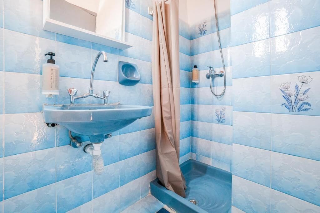 Une salle de bain avec un mur recouvert de carreaux bleus, un lavabo, une douche et des toilettes.