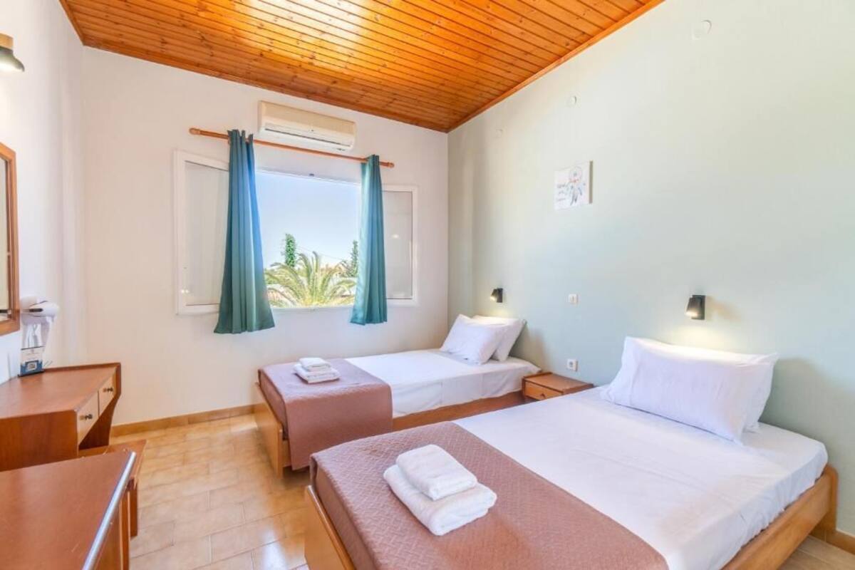 Habitación de hotel con dos camas, techo de madera, ventana con cortinas, escritorio y mesita de noche.