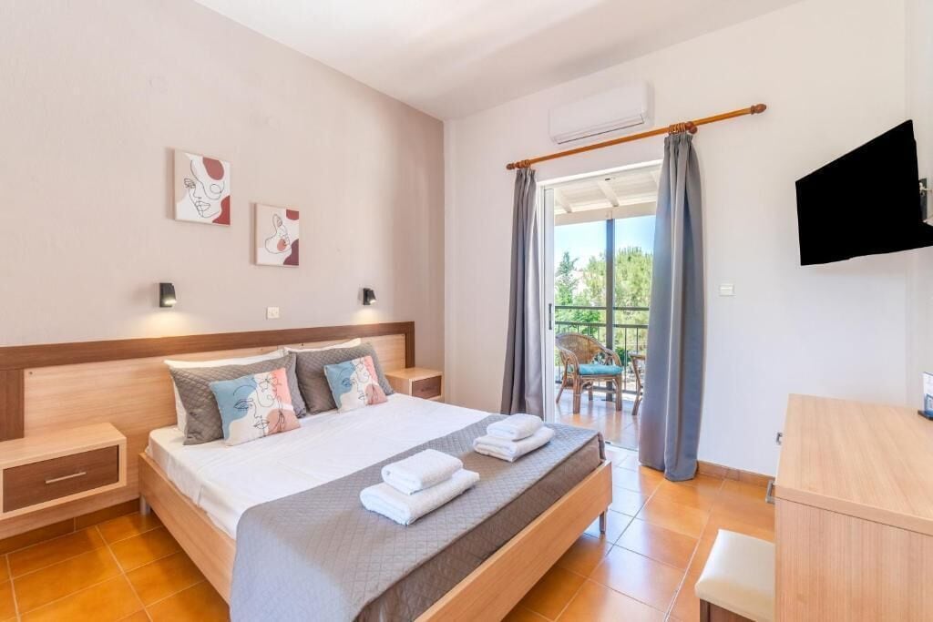 Et hotelværelse med en stor seng, sengeborde, et fjernsyn og en balkon med en stol.