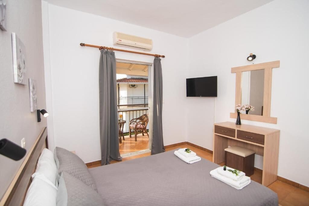 Ein Hotelzimmer mit Bett, Schreibtisch mit Spiegel, Flachbildfernseher und Balkon mit Stuhl und Tisch.