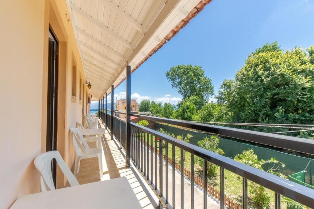 A balcony with white plastic chairs and a view of a river and greenery.