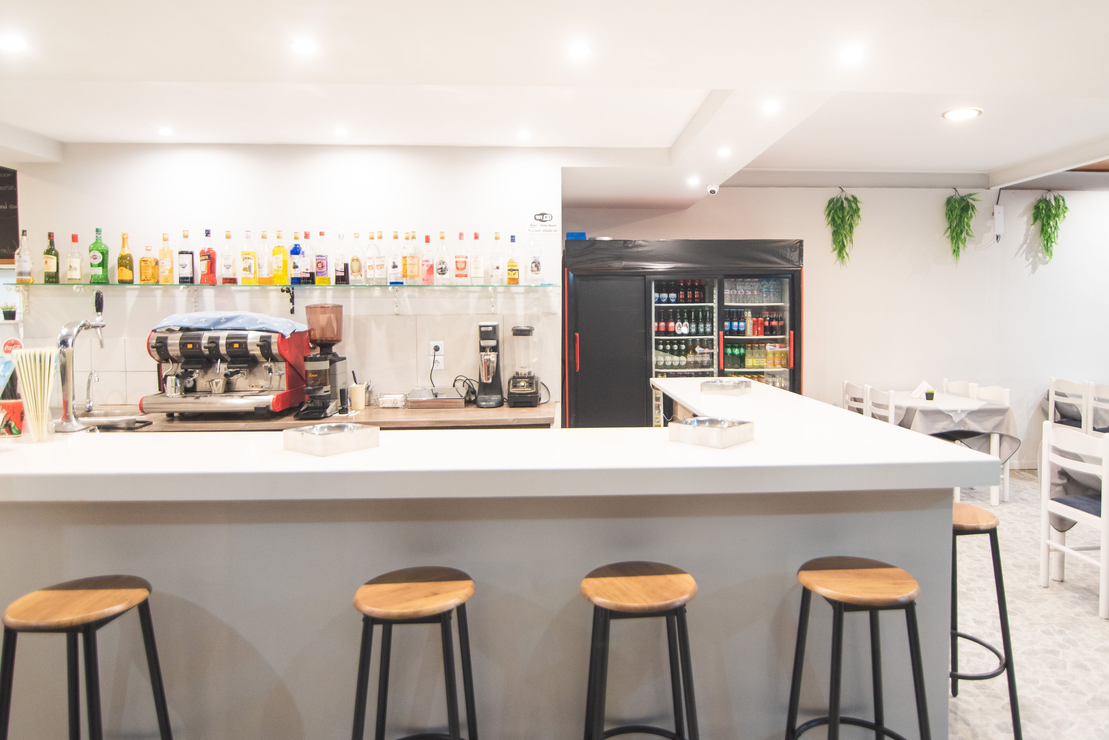 A bar area with stools, a coffee machine, and a refrigerator stocked with beverages.