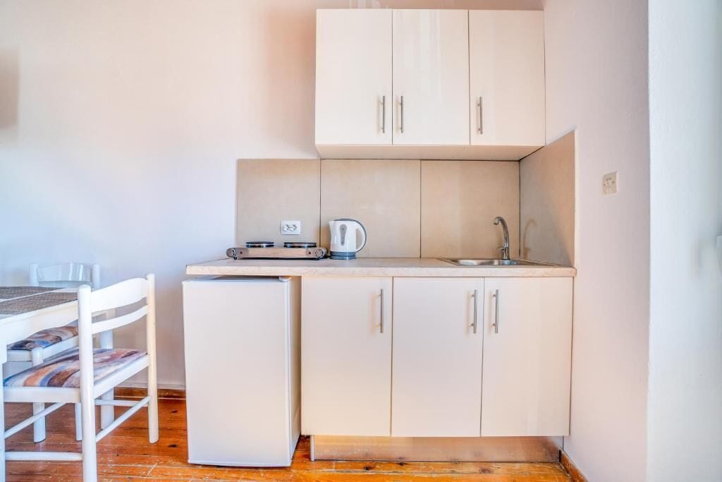 A compact kitchen with a refrigerator, a kettle, and a sink.