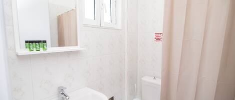 A bathroom with a sink, mirror, toilet, and shower curtain.