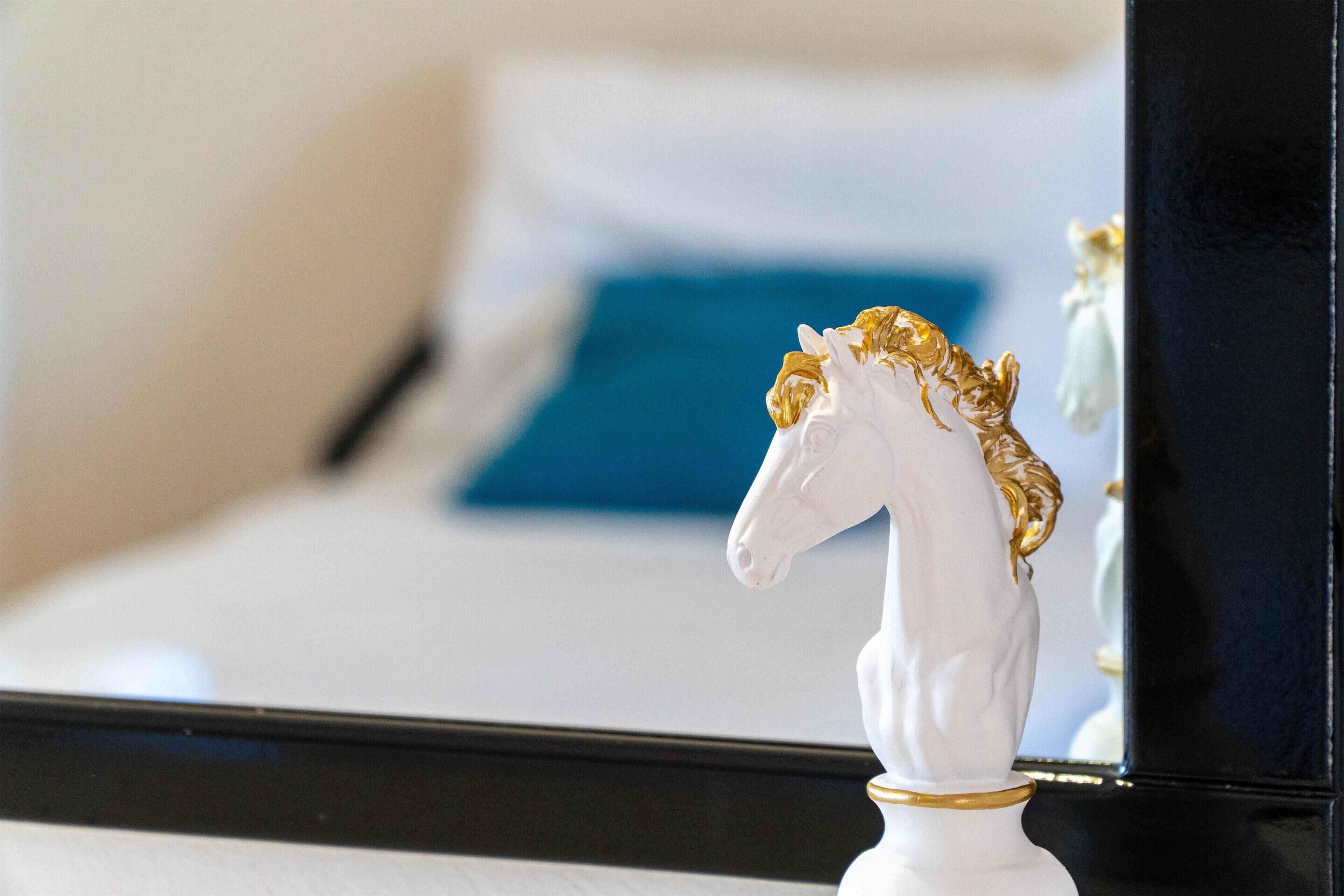 A white horse head statue with a golden mane on a bed with a blue pillow.