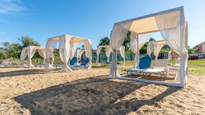 A beach area with white canopies and blue lounge chairs. - Saint Peter Bay Aparthotel by Konnect (Corfu)
