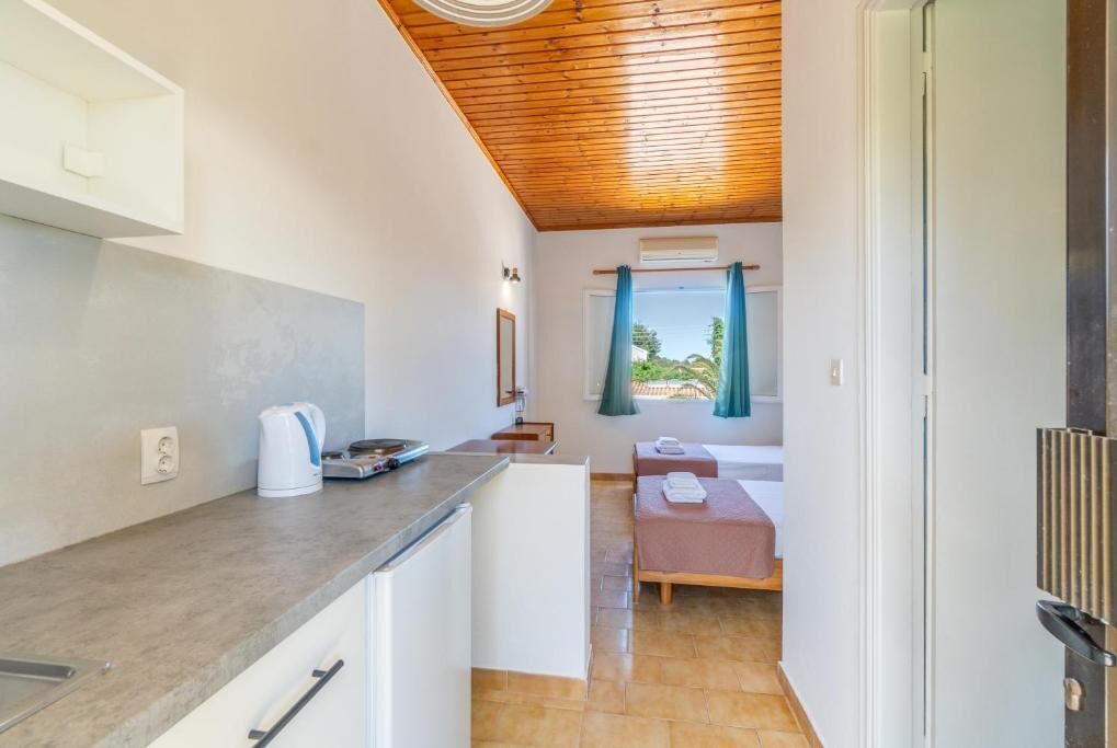 A compact kitchen with a countertop, kettle, and a small dining area with a table and bench.