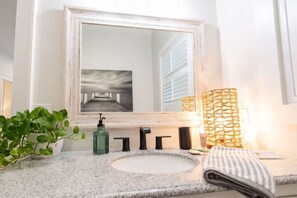 A bathroom with a granite countertop, a round sink, a large mirror, a potted plant, a towel, and a decorative light fixture.