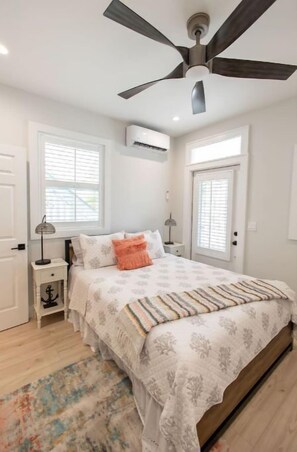 Une chambre à coucher comprenant un lit, un ventilateur de plafond, un appareil de climatisation et une fenêtre avec des stores.