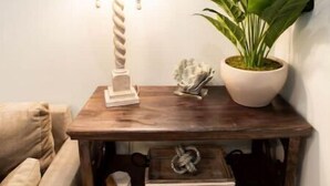 Un coin avec une table de chevet en bois, une lampe, une plante en pot et un petit objet décoratif.