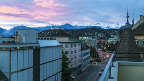 Un paysage urbain avec des bâtiments modernes, une rue animée par la circulation et une chaîne de montagnes en arrière-plan.