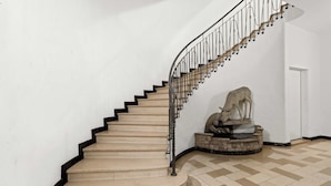 A spiral staircase with beige steps and black railings, leading to a door. A stone sculpture of a deer is placed on a circular platform at the bottom of the stairs. - Cozy Central Lucerne Apartment with Balcony (Luzern)