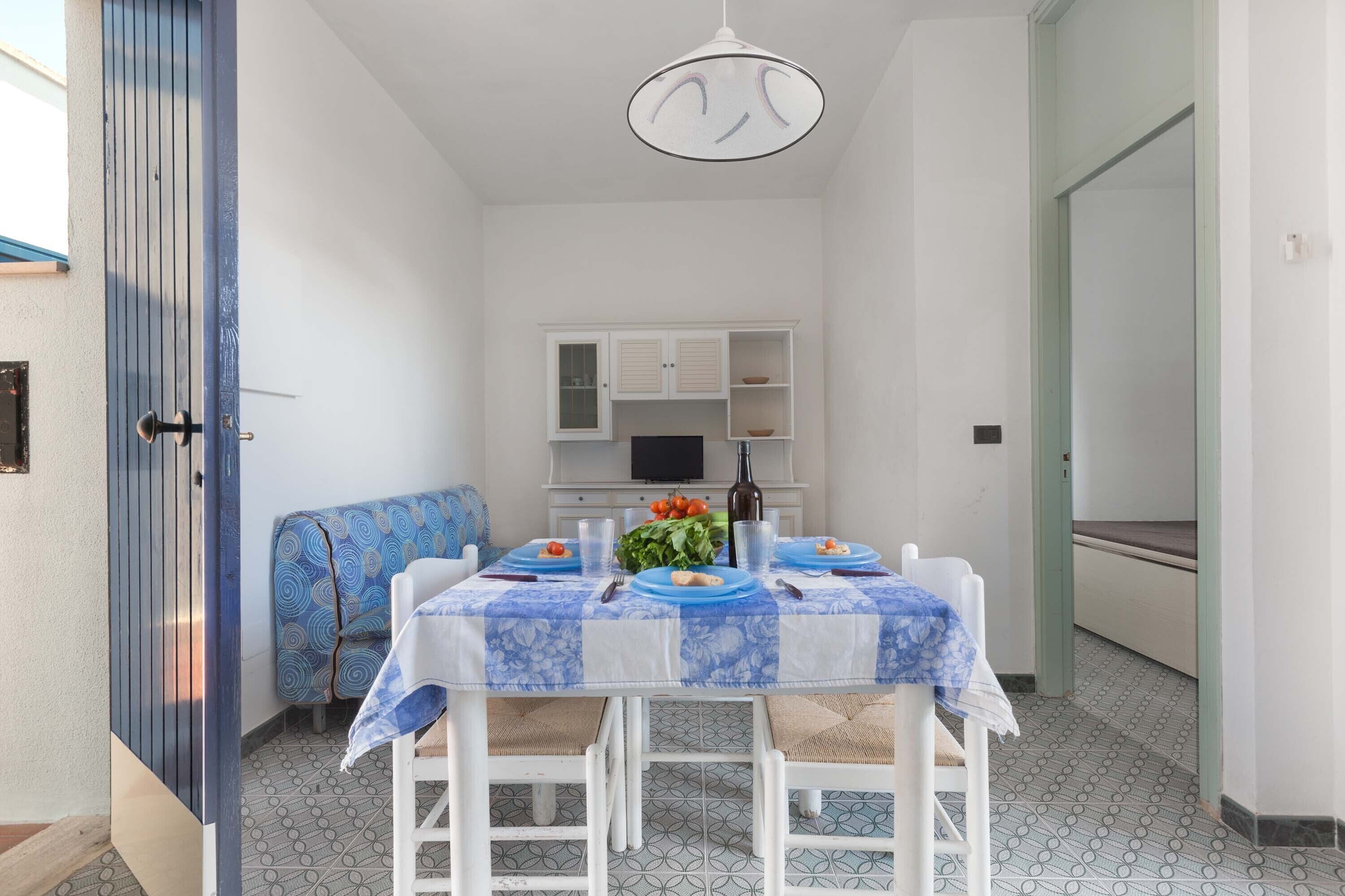 A dining area with a table set for two, a sofa, and a kitchen in the background.