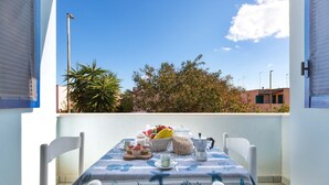 Un balcon avec une table préparée pour le petit-déjeuner, comprenant des fruits, des viennoiseries et une cafetière.