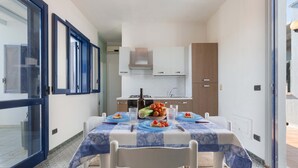 Un coin repas avec une table dressée pour quatre personnes, une cuisine en arrière-plan et une grande fenêtre sur la gauche.