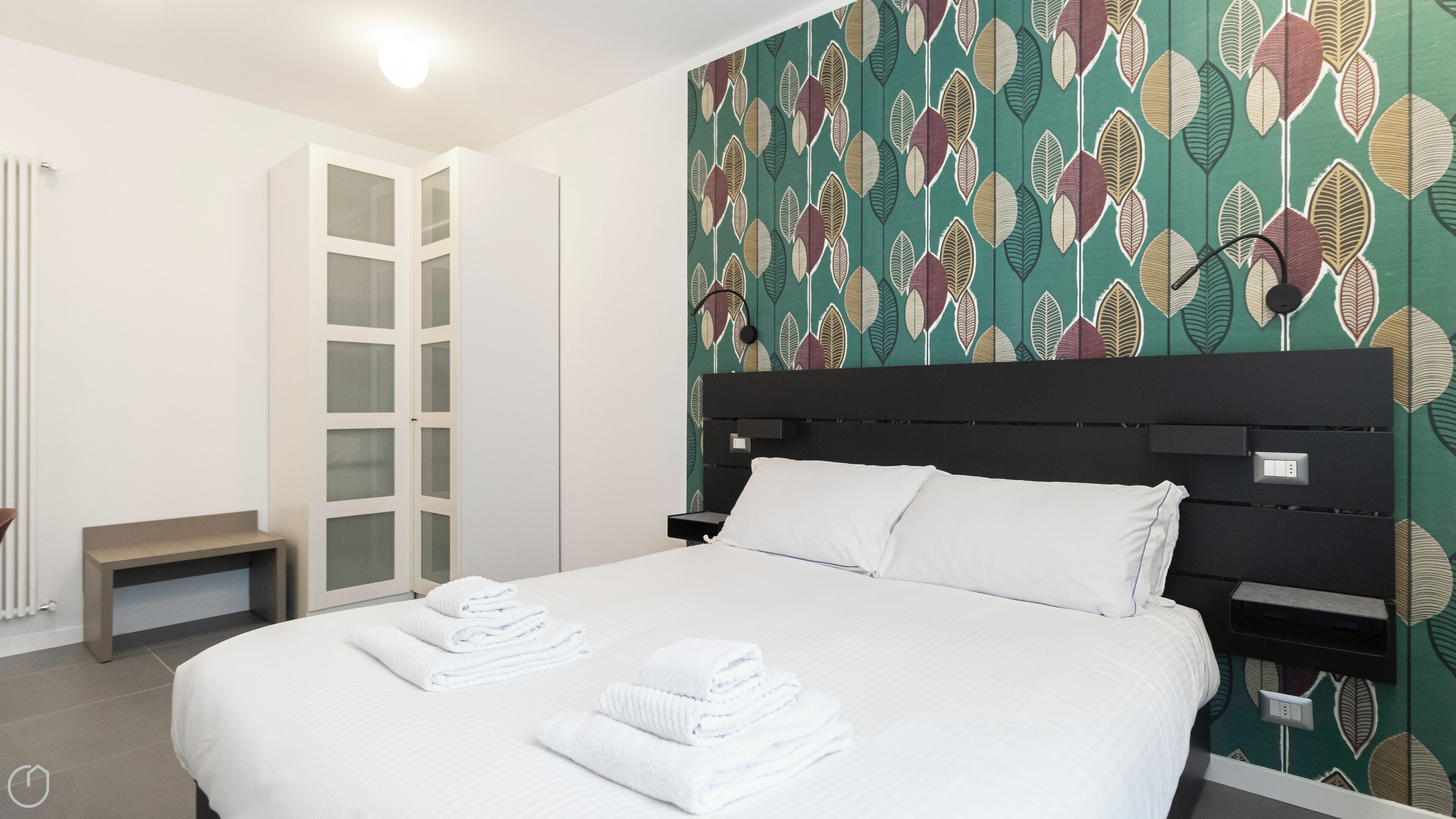 A neatly made bed with white linens and towels, a black headboard, and a wall with a leaf pattern.