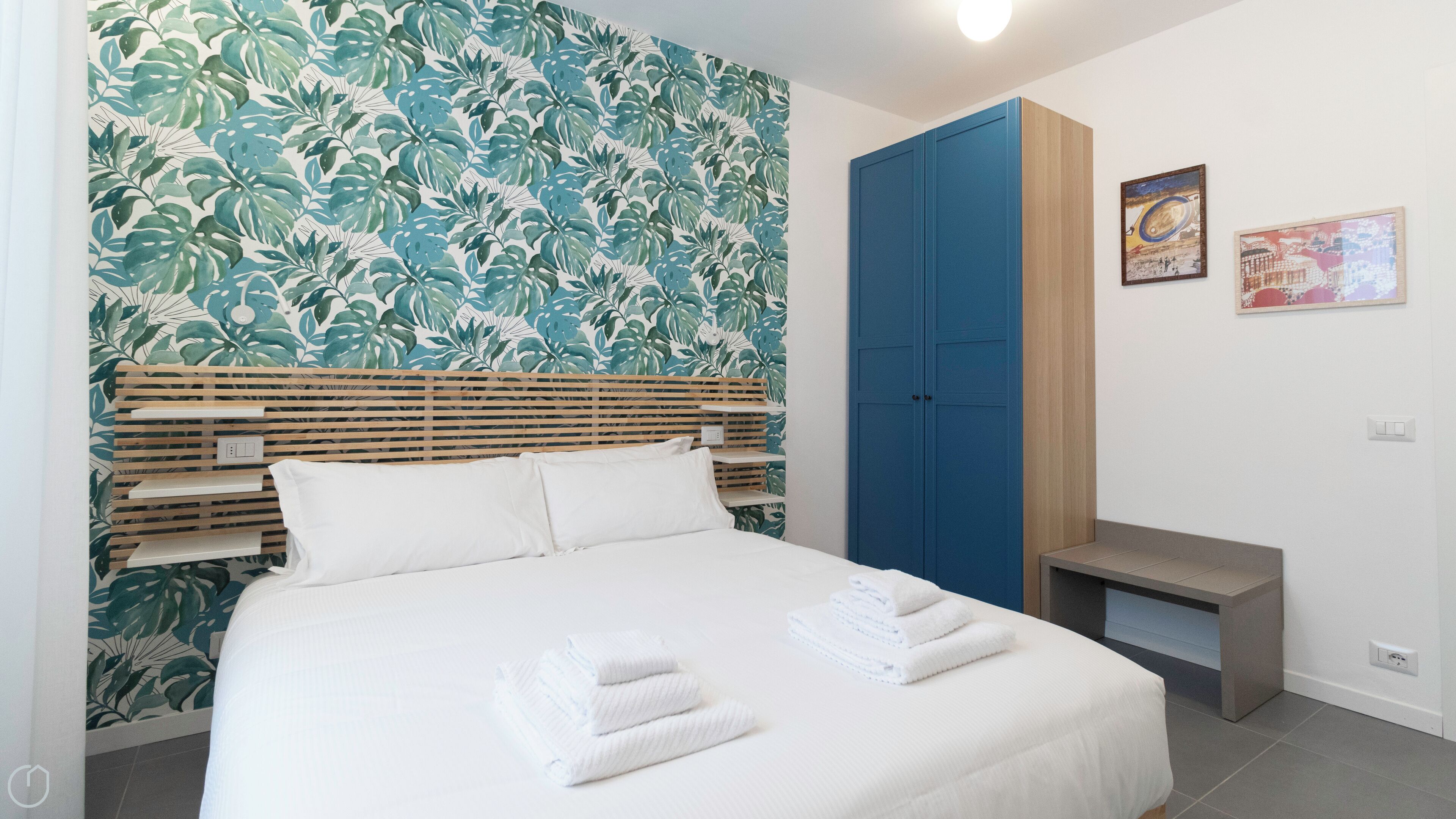 A bedroom with a bed, a wooden headboard, a blue wardrobe, and a small bench.